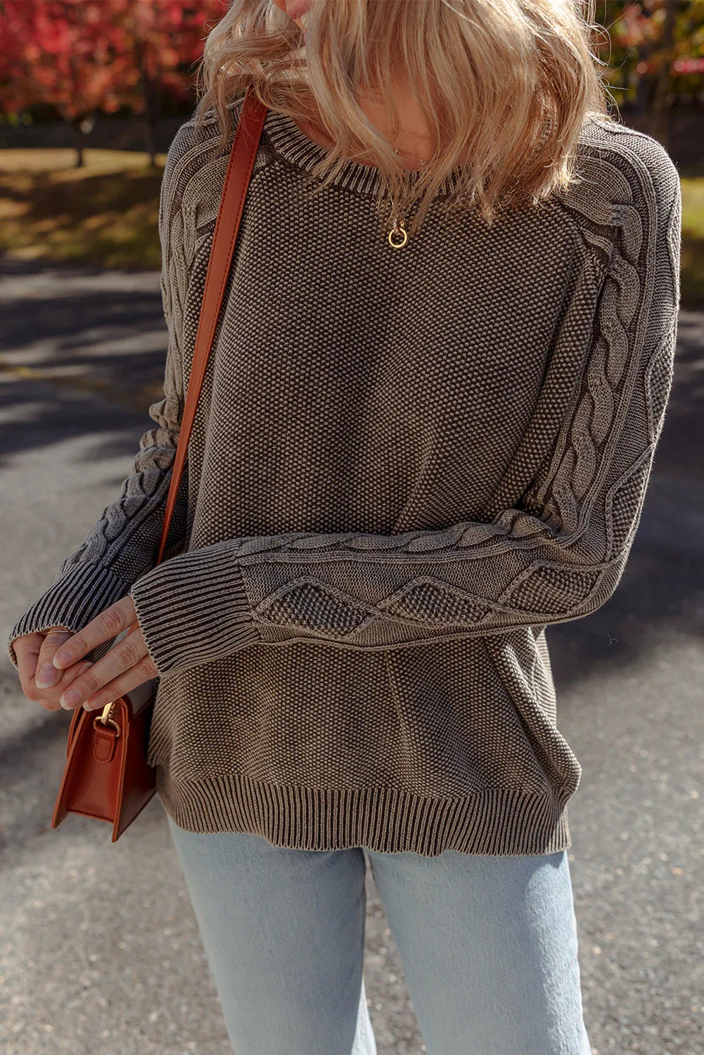 Woman wearing a textured knit sweater with cable sleeves and light wash jeans outdoors.