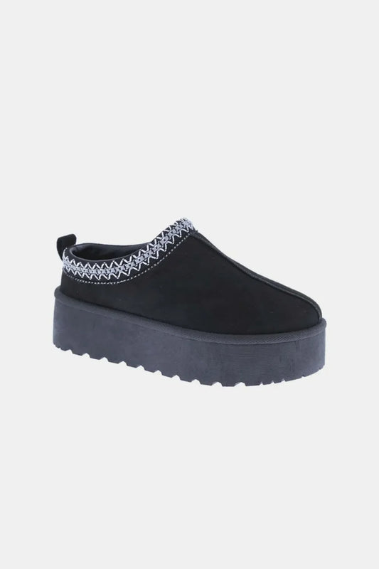 Black platform slip-on shoe with zigzag trim and textured sole on white background