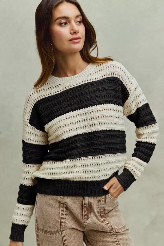Woman wearing a black and cream striped knit sweater with casual beige pants.