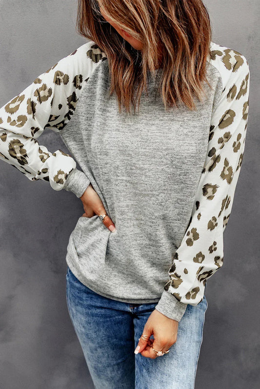 Woman wearing a grey pullover with leopard print sleeves and blue jeans