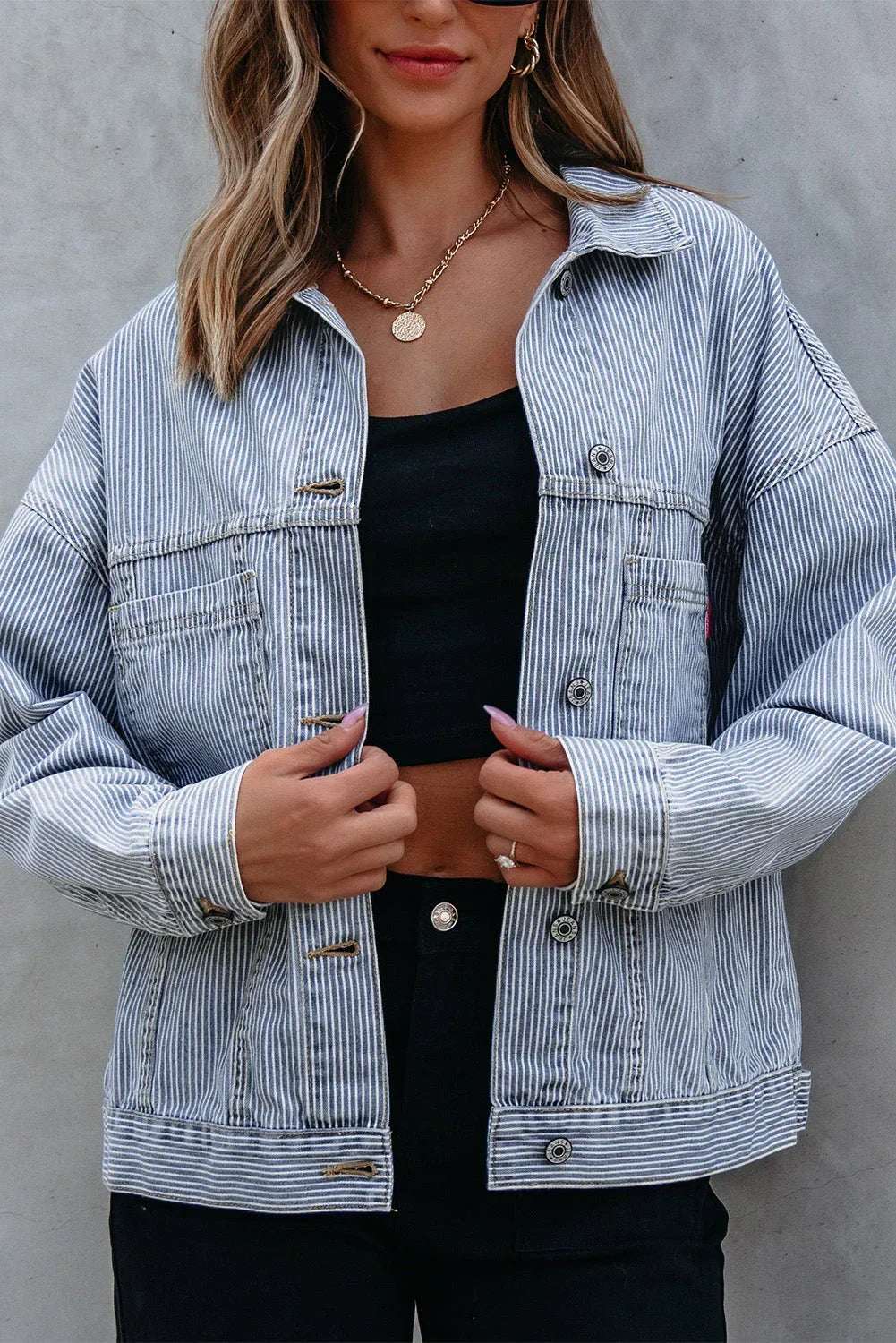 Woman wearing a blue and white striped denim jacket over a black crop top