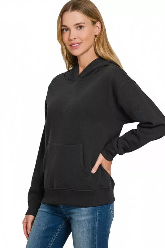 Woman in black hoodie and blue jeans posing against white background, casual fashion style
