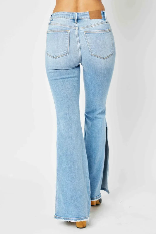 Back view of light wash high-rise flare jeans with raw hem and leg slits on a model