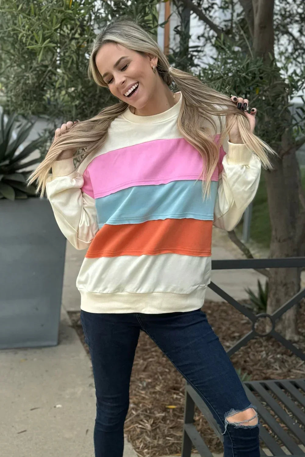 Woman outdoors in a pastel color block sweatshirt and dark ripped skinny jeans