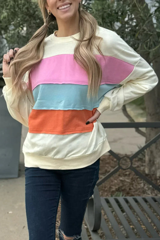 Woman wearing a pastel colorblock sweatshirt with pink, blue, and orange stripes outdoors