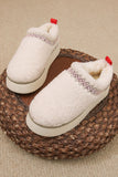 Cream sherpa slip-on platform slippers with red pull tabs and decorative stitching, on woven pouf