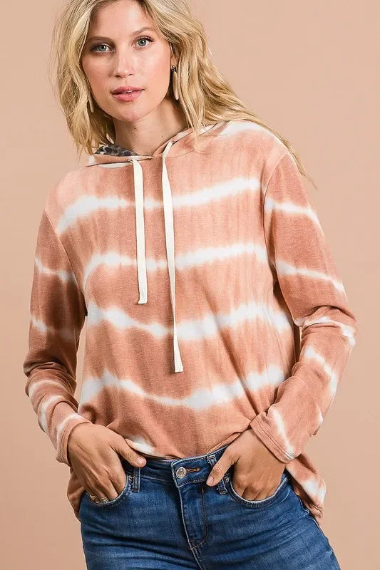 Woman wearing a relaxed fit, long sleeve, tie-dye hoodie with drawstring and blue jeans.