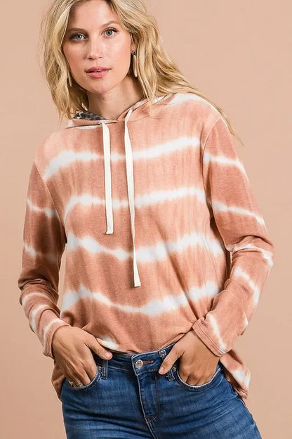 Woman wearing a relaxed fit, long sleeve, tie-dye hoodie with drawstring and blue jeans.