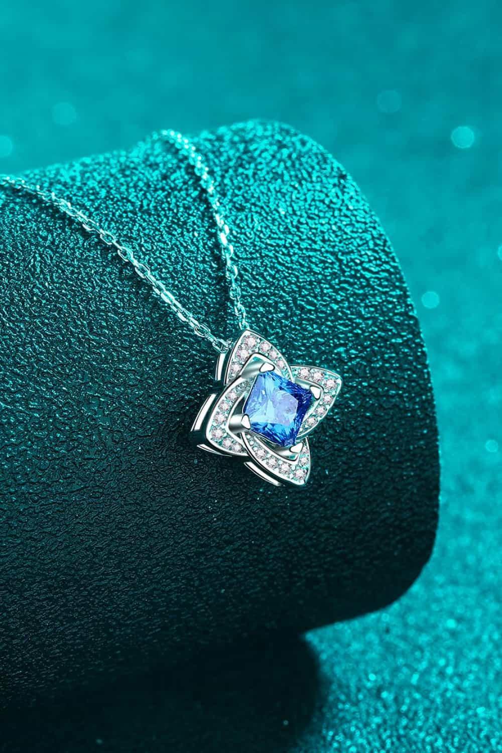 Silver necklace with a blue gemstone pendant and diamond accents, displayed on teal background.