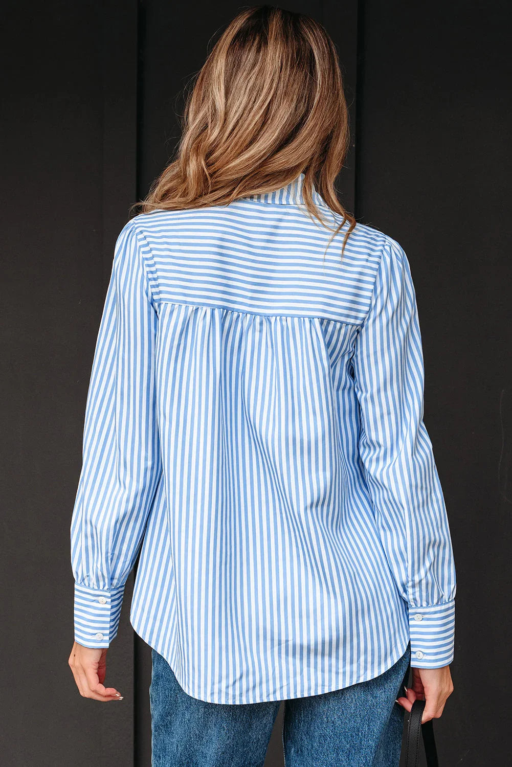 Woman wearing a blue and white striped long sleeve button-up shirt and jeans, shown from the back.