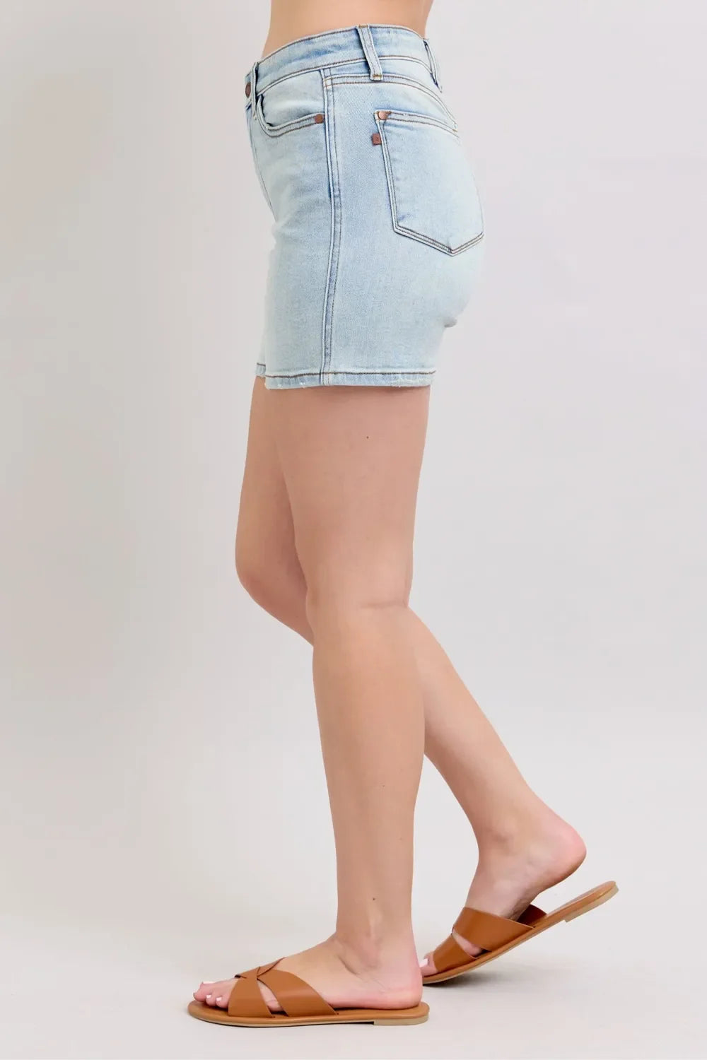 Woman wearing light wash denim shorts and brown sandals, side profile on neutral background