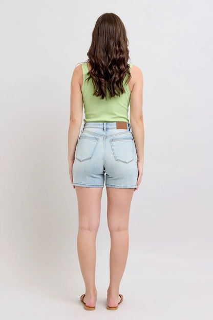 Woman in sleeveless green top and light denim shorts, standing against white background