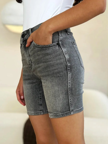 Woman wearing high-rise grey denim shorts with a casual white top, hand in pocket