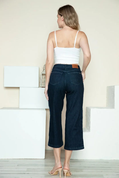 Woman in a white camisole and dark wide-leg cropped jeans standing indoors, back view