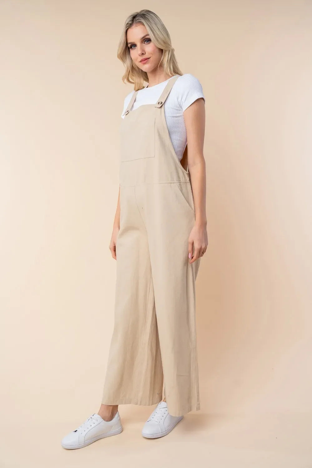 Woman wearing beige wide-leg jumpsuit over white ribbed t-shirt and white sneakers