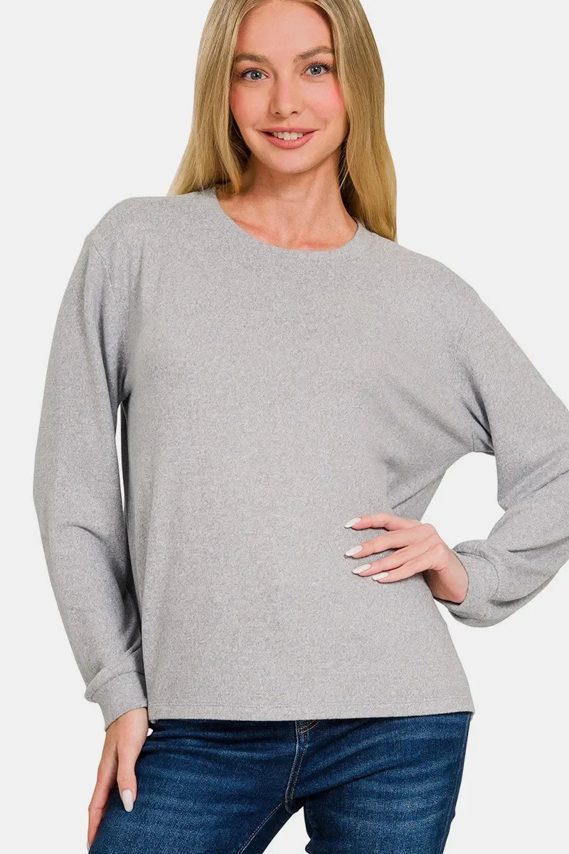 Woman wearing a light grey long sleeve pullover top with blue jeans.