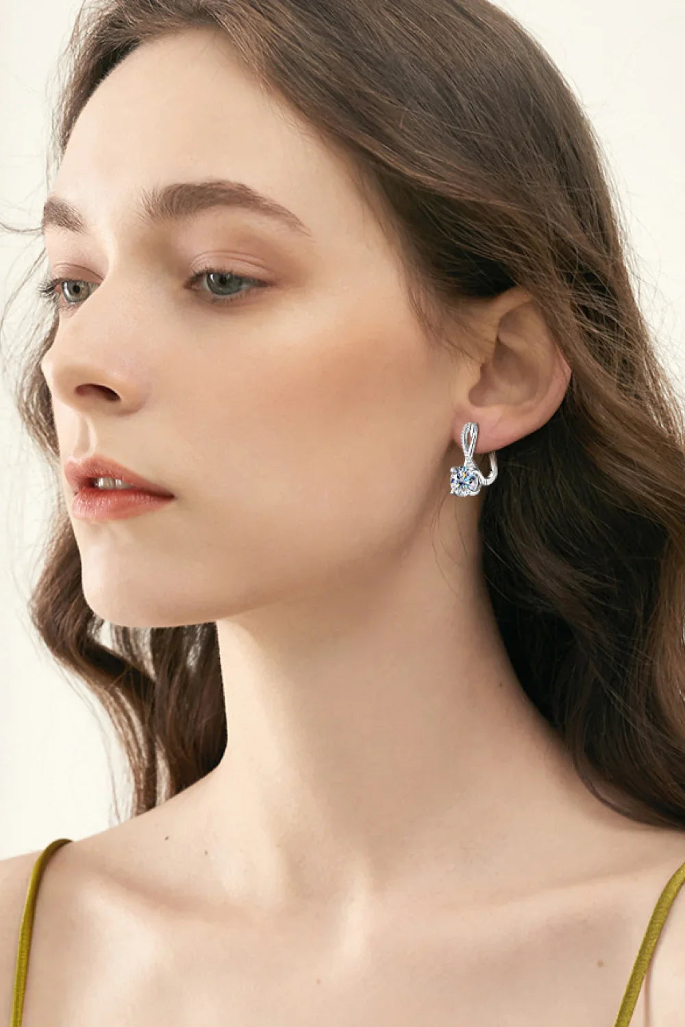 Woman wearing elegant silver drop earrings with crystal detail, neutral background