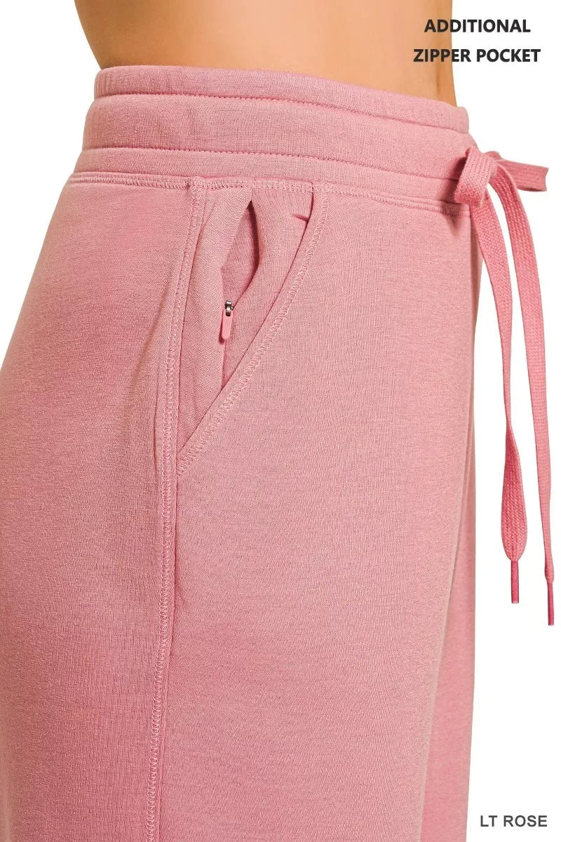 Light rose pink women's jogger pants with drawstring waist and zipper pocket detail.
