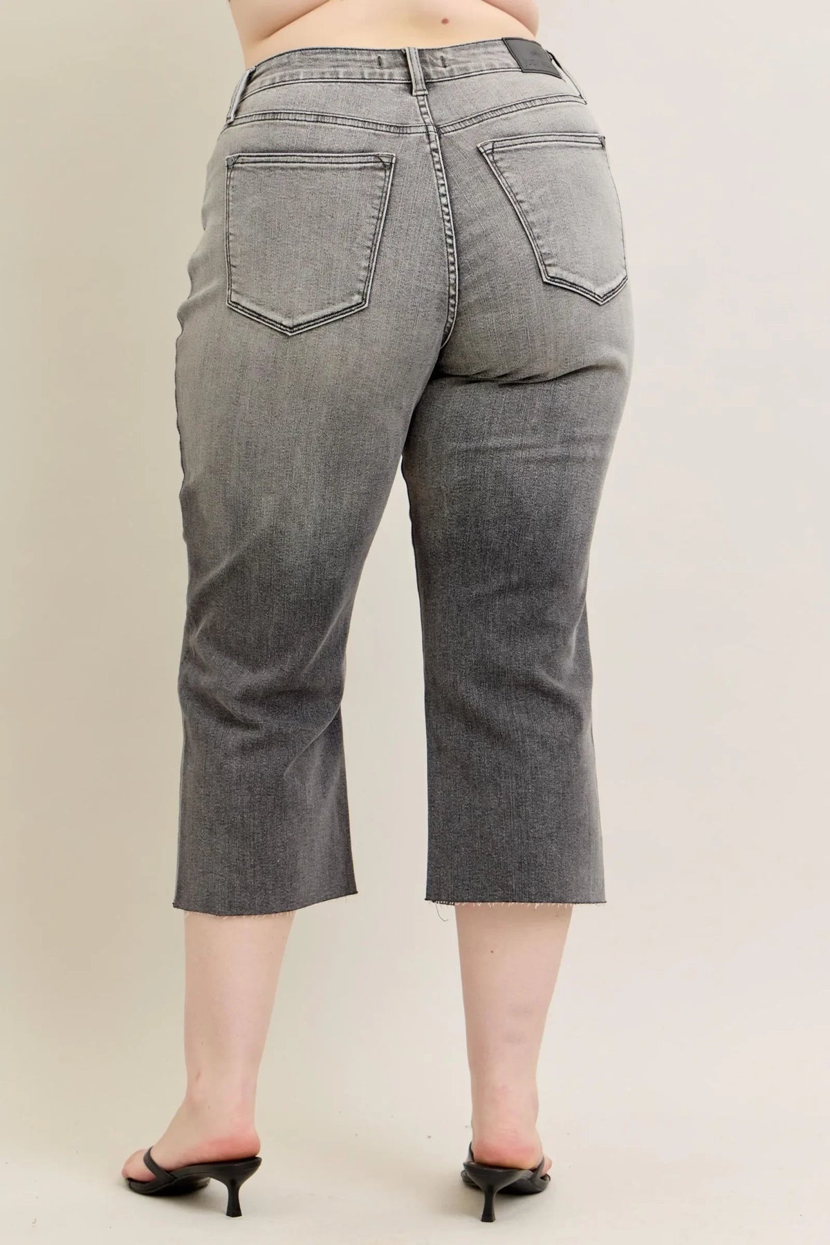 Back view of cropped grey denim jeans with raw hem and high waist on model.