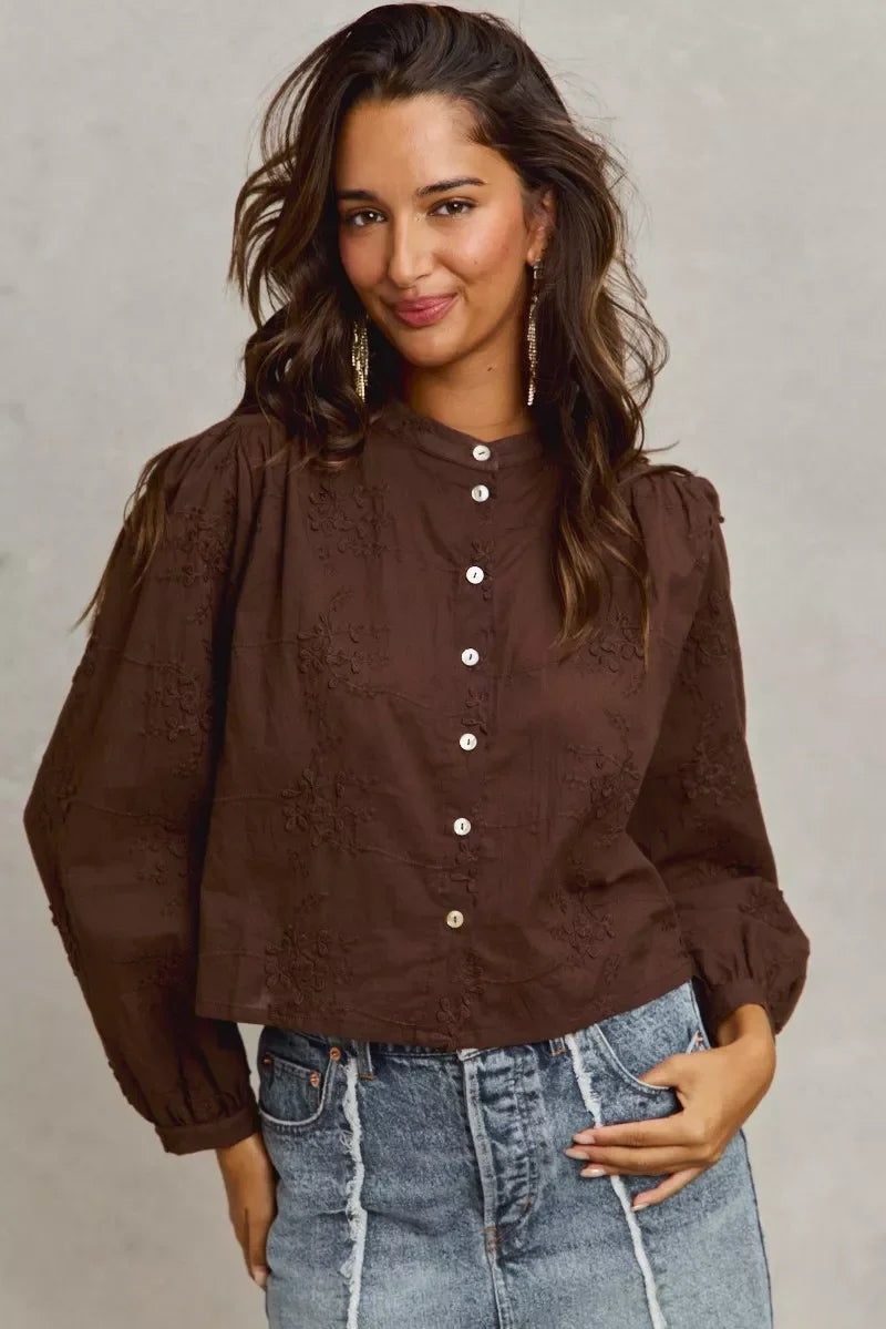 Woman wearing a brown long sleeve embroidered blouse and high-waisted denim jeans