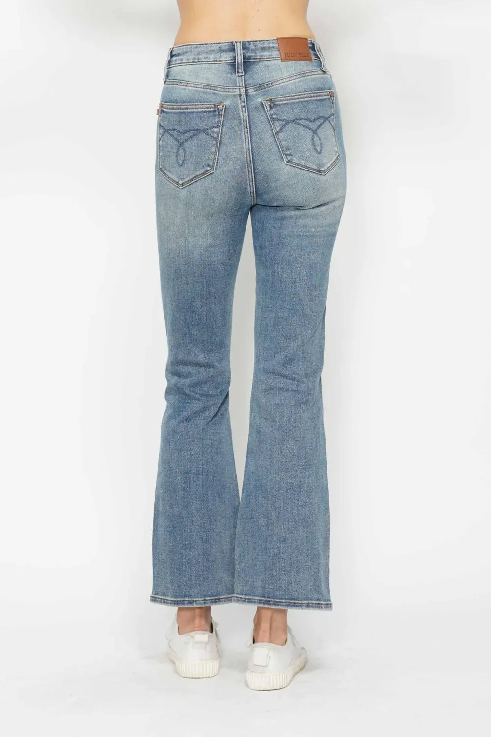 Back view of woman wearing light blue flared jeans with back pockets and white sneakers