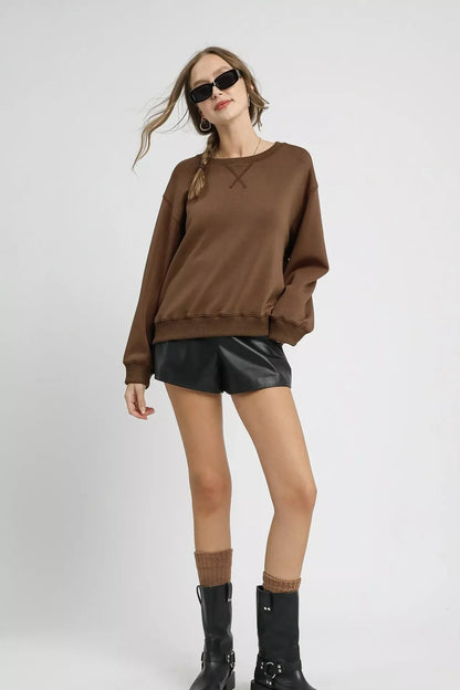 Woman wearing mocha brown sweatshirt, black leather shorts, black boots, and sunglasses.