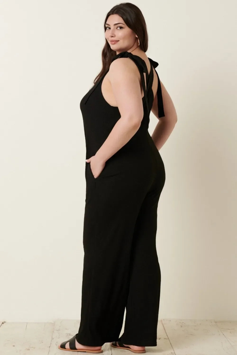 Woman wearing a black sleeveless jumpsuit with tie shoulder straps and wide legs