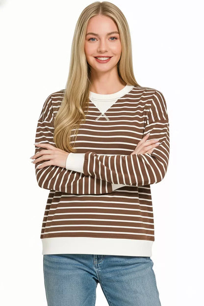 Woman wearing a brown and white striped long sleeve sweater with relaxed fit and blue jeans