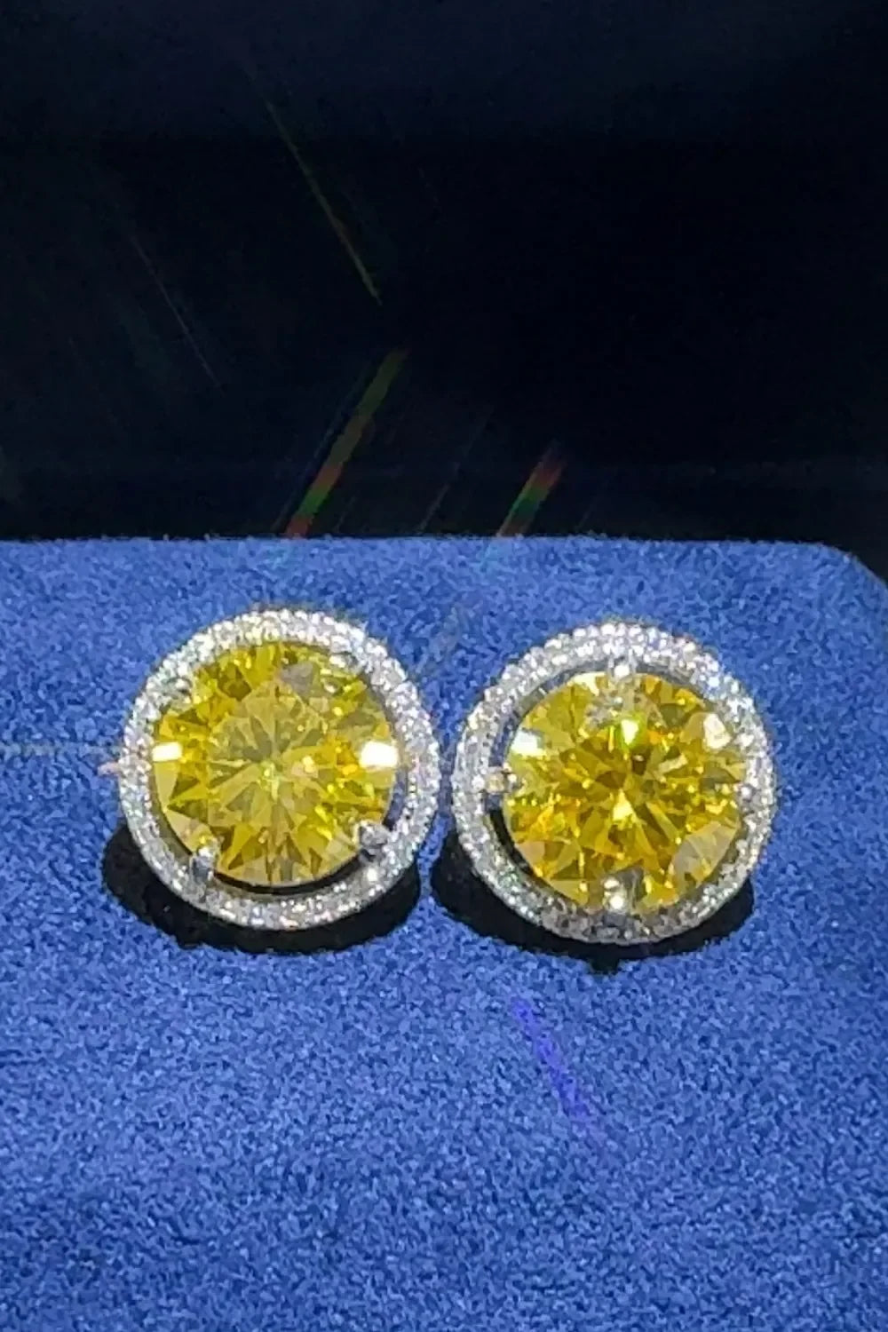 Round yellow gemstone stud earrings with diamond halo on blue fabric background