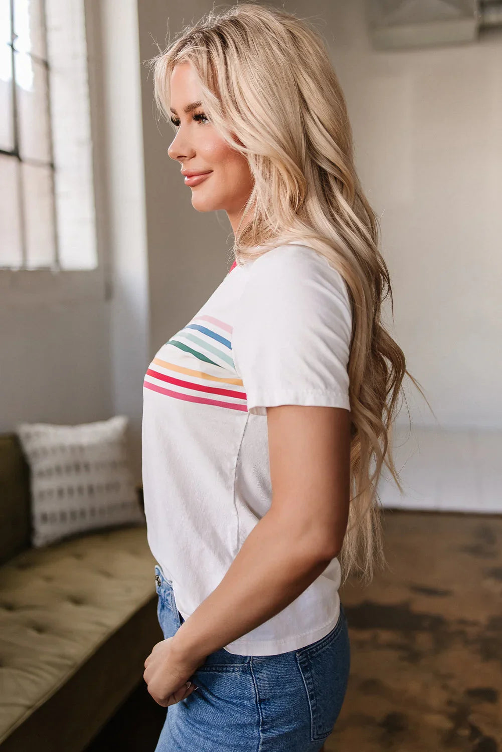 Woman in white t-shirt with colorful stripes and blue jeans standing indoors