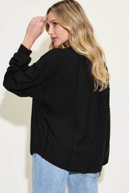 Woman wearing a loose black textured blouse and light wash jeans, viewed from behind