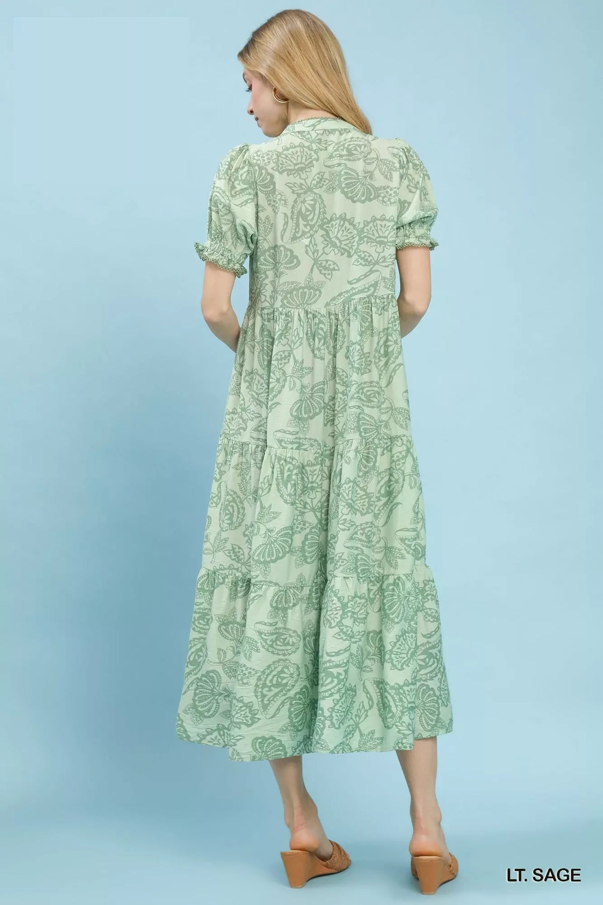 back of a Woman wearing an Umgee Paisley Print Tiered Midi Dress on a blue background and brown slip on heeled sandals