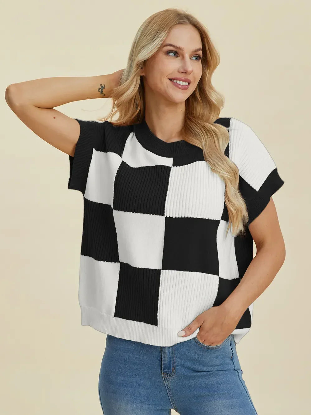 Woman wearing a black and white checkered knit short sleeve top with blue jeans