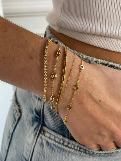 Woman wearing layered gold bracelets and denim jeans, showcasing modern minimal jewelry.