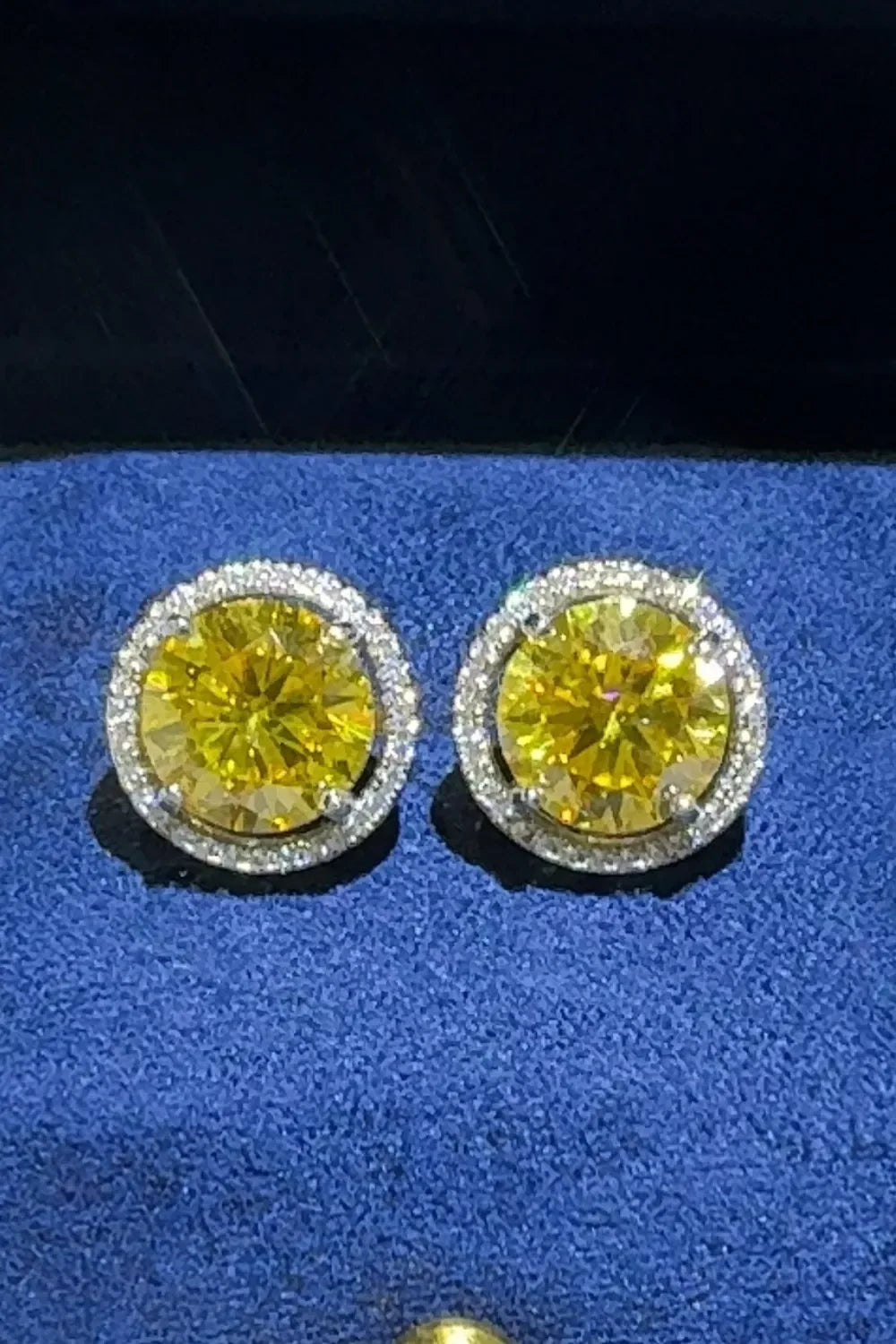 Yellow gemstone stud earrings with diamond halos on a blue fabric background