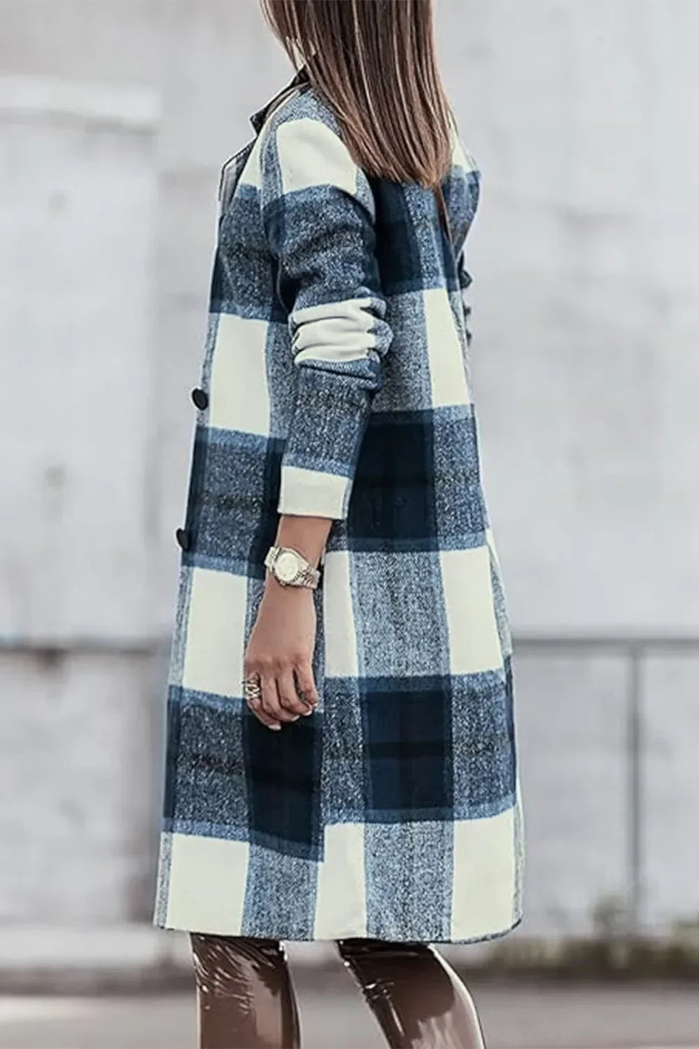 Woman wearing a long blue and white plaid coat with rolled sleeves, standing outdoors.