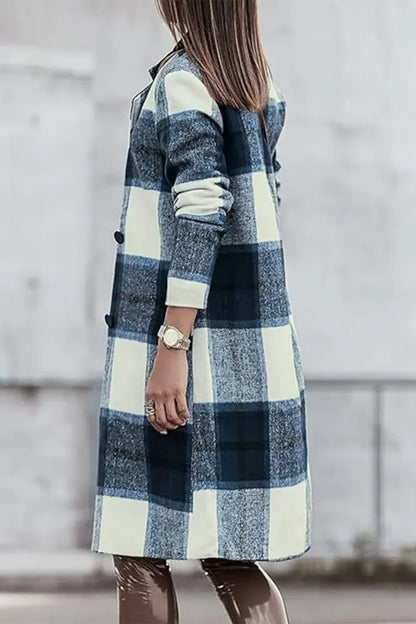 Woman wearing a long blue and white plaid coat with rolled sleeves, standing outdoors.