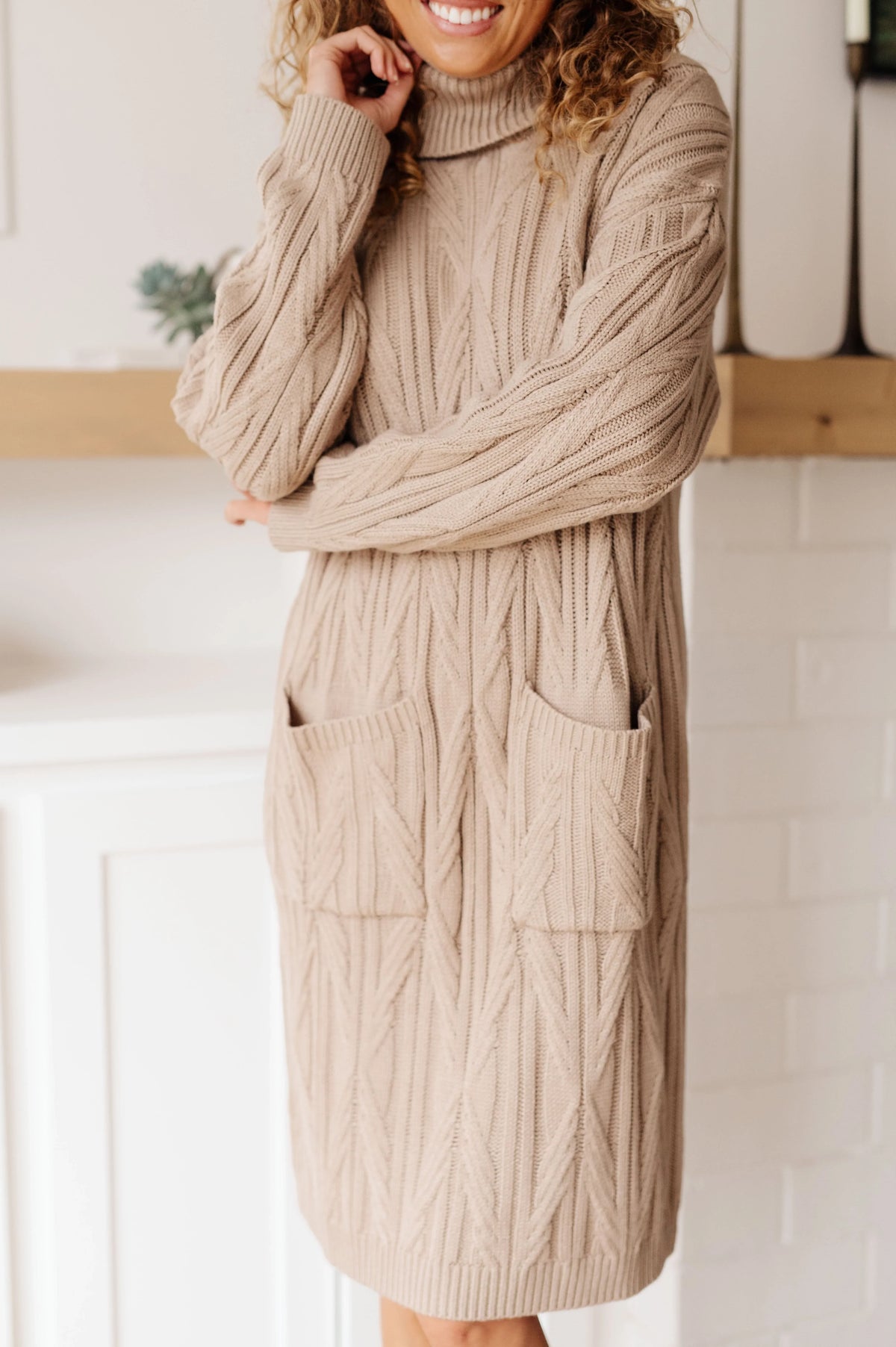 Woman wearing a beige cable knit sweater dress with turtleneck and front pockets