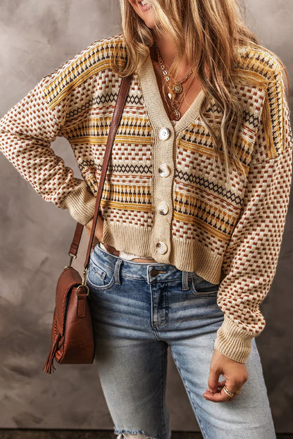 Woman wearing a patterned knit cardigan with large buttons, blue jeans, and a brown crossbody bag