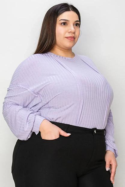 Woman in light purple ribbed long sleeve blouse and black pants against neutral background