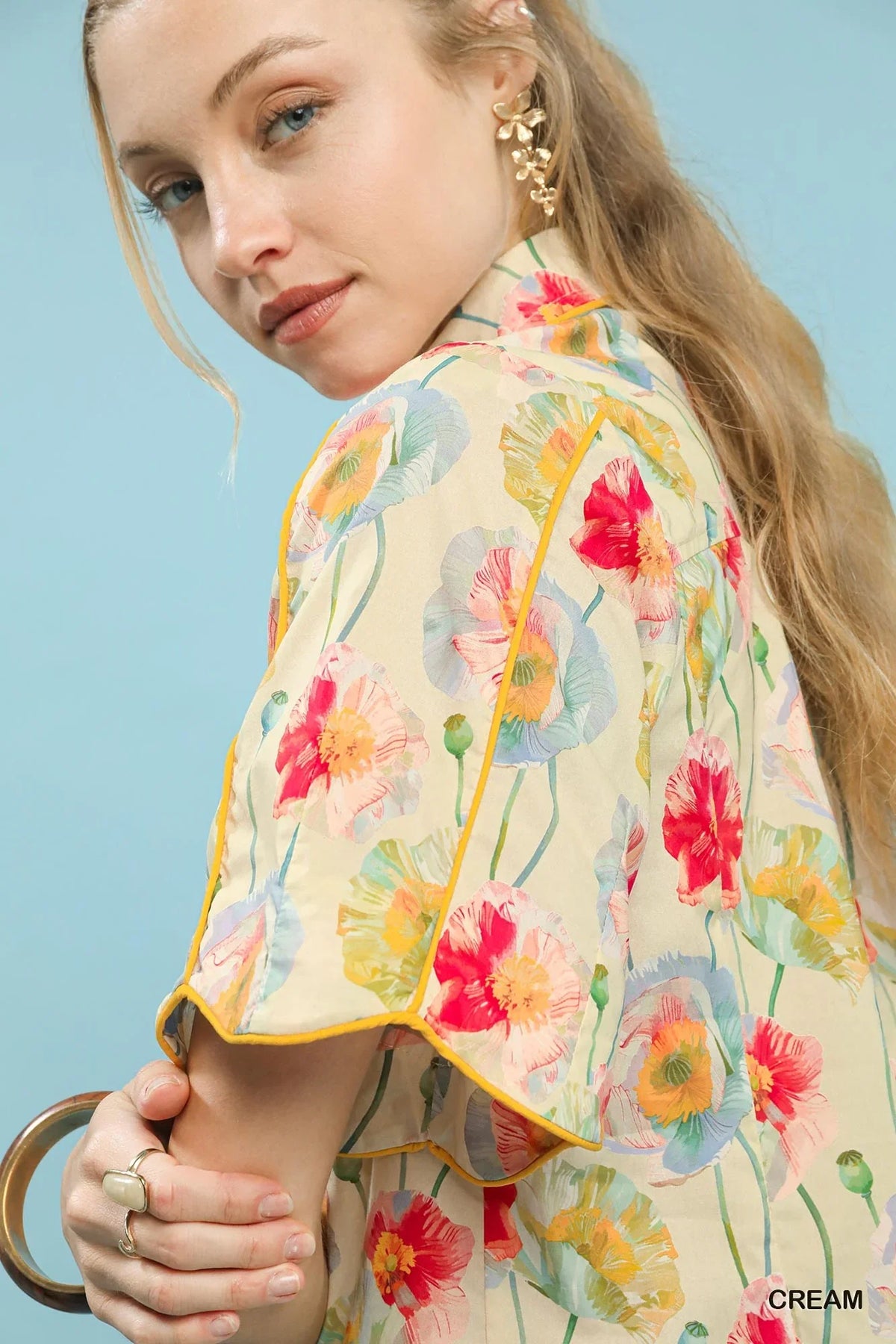 Woman wearing a cream floral blouse with colorful poppy print and gold earrings