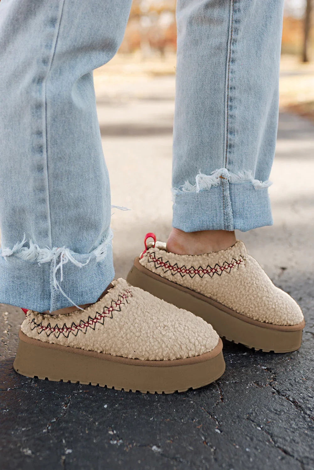 Beige fleece slip-on platform shoes with red stitching, paired with light blue frayed jeans