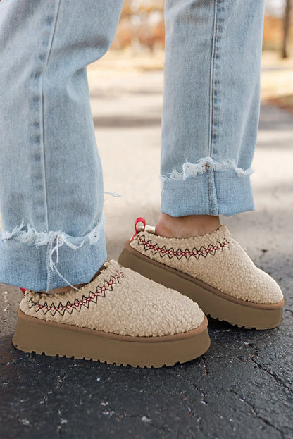 Beige fleece slip-on platform shoes with red stitching, paired with light blue frayed jeans