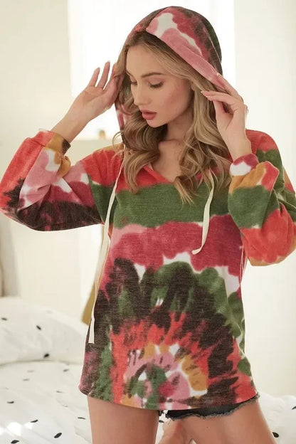 Woman wearing a colorful tie-dye hoodie with drawstrings, standing in a bright bedroom.