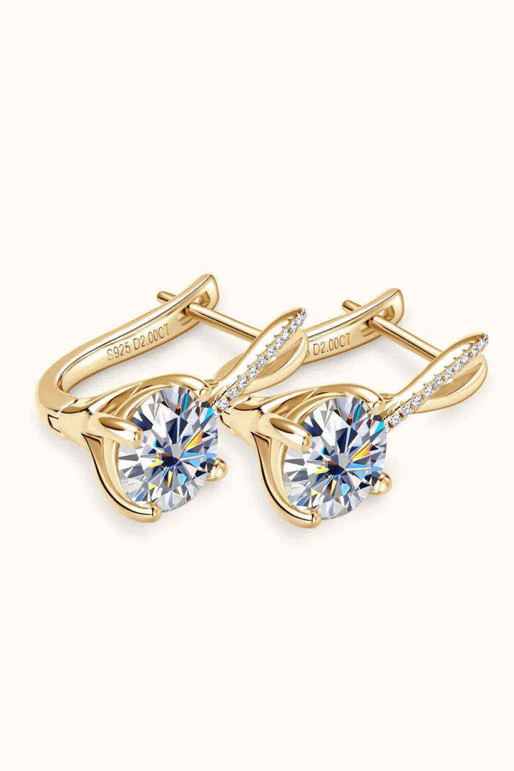 Gold stud earrings with large round clear gemstones and pavé accents on a cream background
