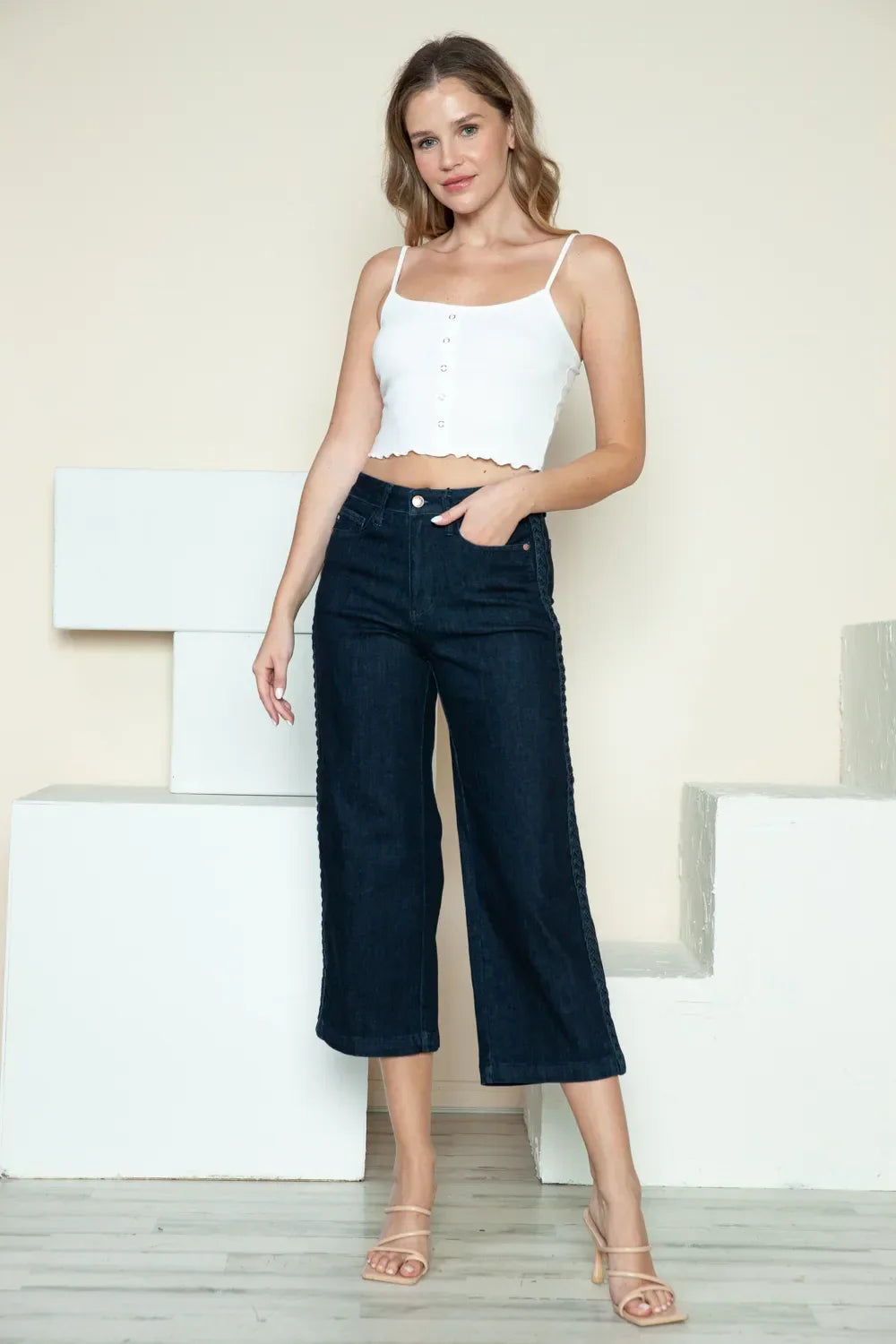 Woman in a white cropped tank top and wide leg dark denim jeans standing indoors