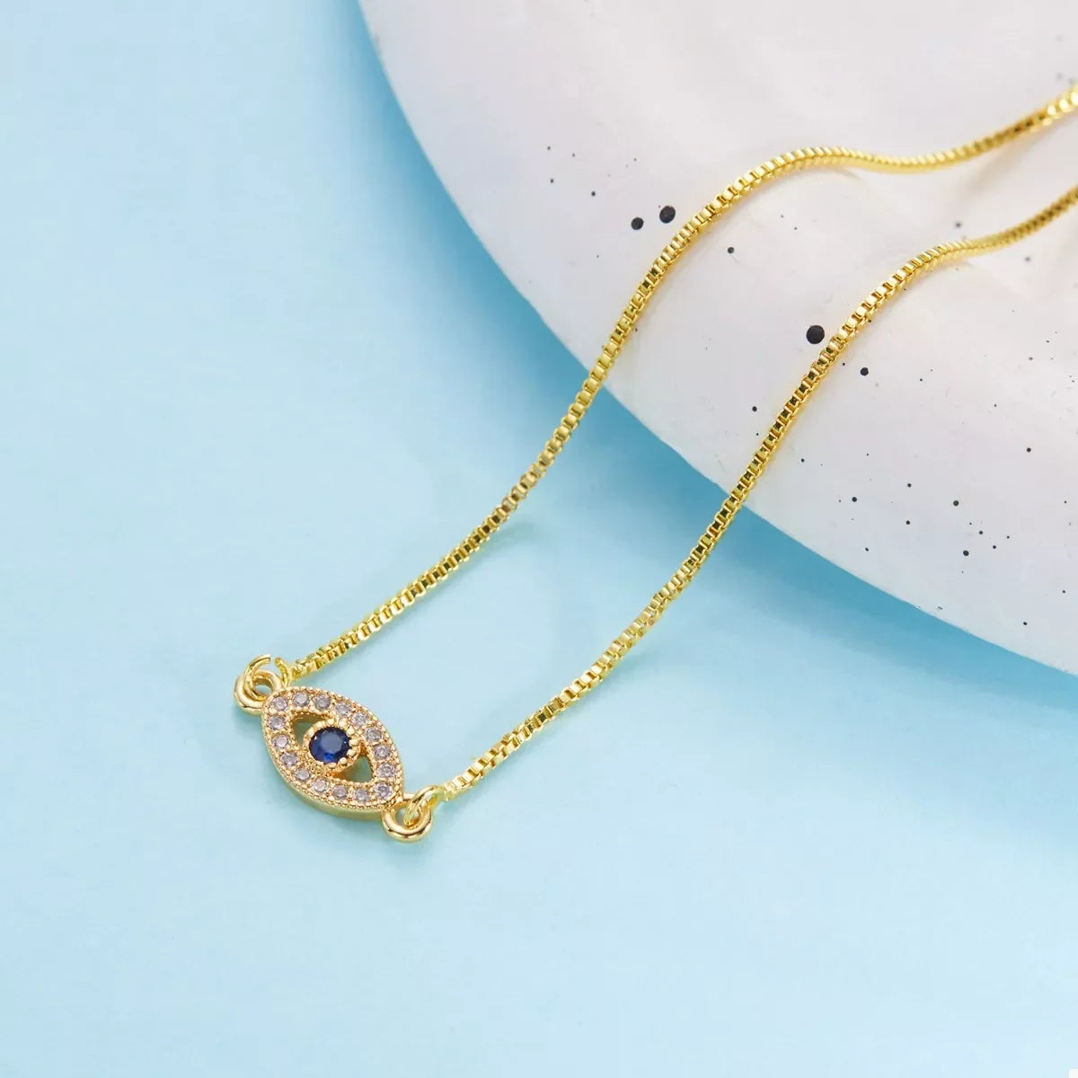 Gold chain necklace with blue evil eye pendant and crystal accents on blue background
