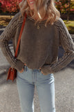 Woman wearing a taupe knit sweater with cable sleeves and light-wash jeans outdoors