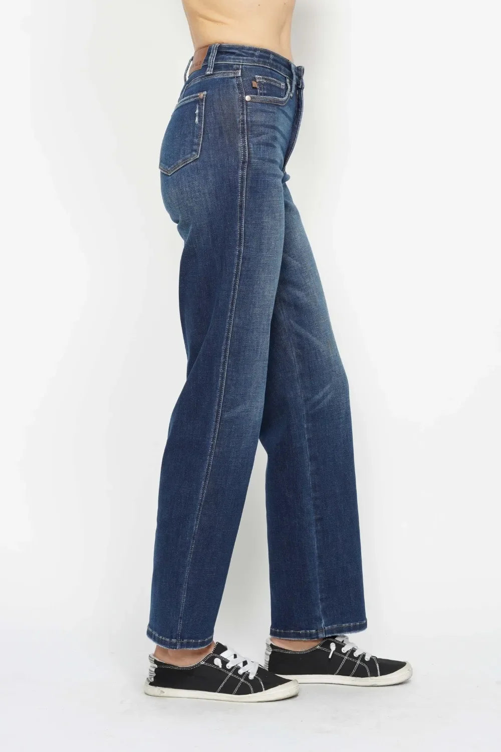 Woman in high-waisted wide-leg blue jeans and black sneakers, side view on white background