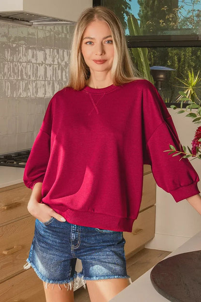 Woman in a relaxed red sweatshirt and denim shorts standing in a modern kitchen